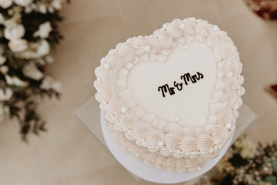 Heart-shaped wedding cake with 'Mr & Mrs' on top, surrounded by flowers - @hellodarlingweddingphotography 